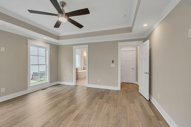 unfurnished bedroom with ceiling fan, light wood-type flooring, a tray ceiling, and connected bathroom