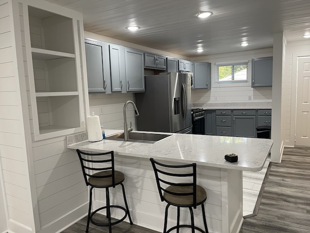 kitchen with sink, kitchen peninsula, stainless steel refrigerator with ice dispenser, dark wood-type flooring, and a breakfast bar