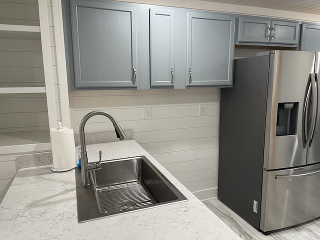 kitchen featuring light wood-type flooring, wooden walls, sink, stainless steel fridge with ice dispenser, and gray cabinetry