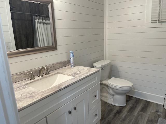 bathroom with wooden walls, toilet, a shower with curtain, wood-type flooring, and vanity