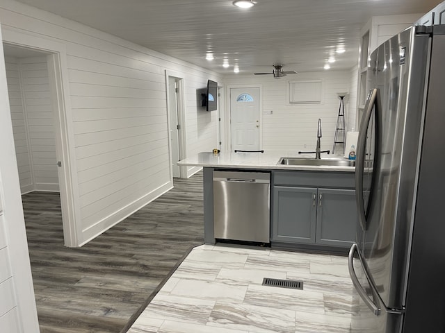 kitchen featuring wood walls, appliances with stainless steel finishes, wood-type flooring, sink, and ceiling fan