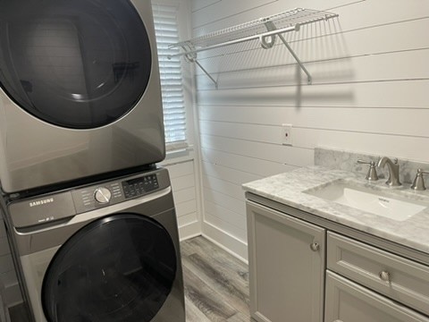 clothes washing area featuring cabinets, hardwood / wood-style floors, wooden walls, stacked washer and clothes dryer, and sink