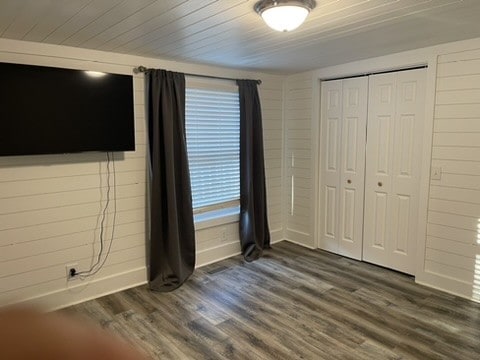 unfurnished bedroom featuring dark wood-type flooring, a closet, and wood walls