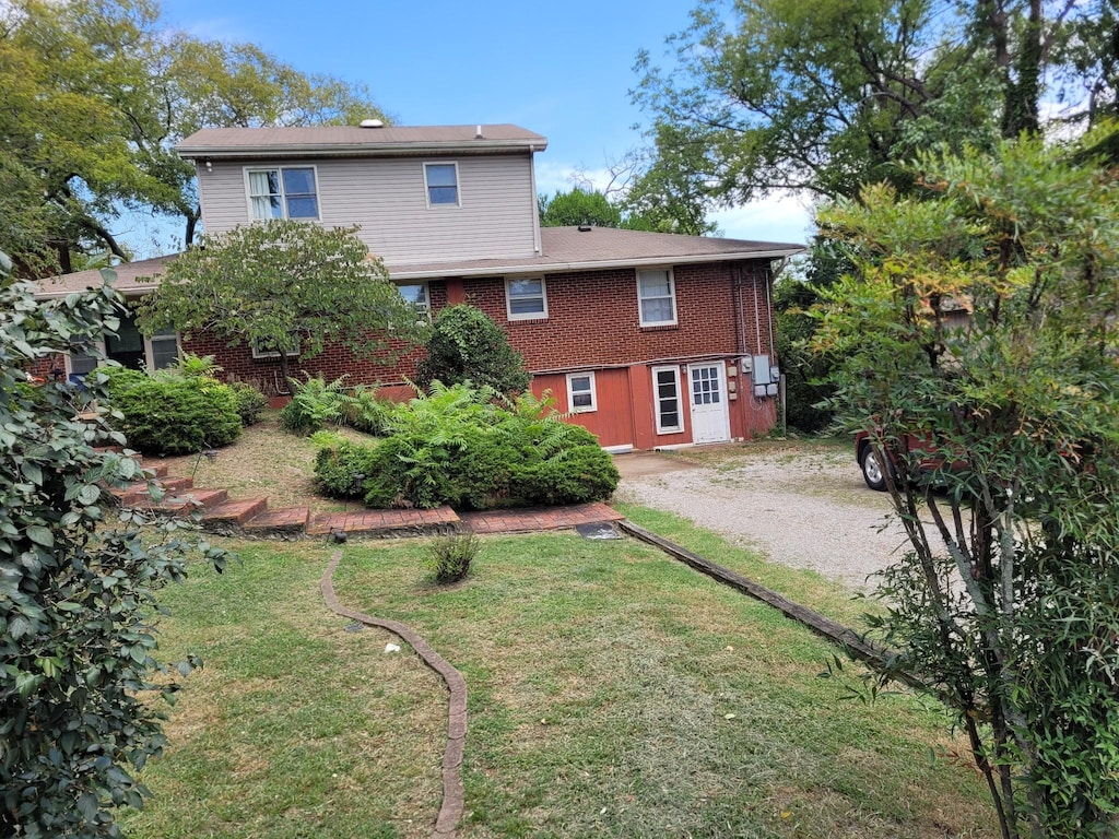 rear view of property featuring driveway, brick siding, and a lawn