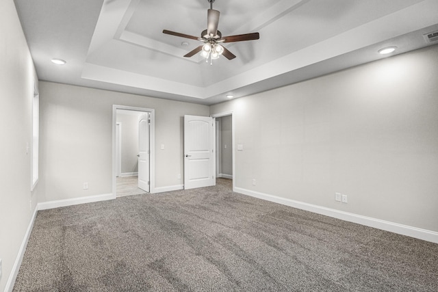 unfurnished bedroom with a tray ceiling, ceiling fan, carpet, and ensuite bathroom