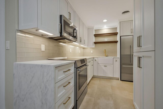 kitchen with appliances with stainless steel finishes, backsplash, sink, white cabinets, and light tile patterned flooring