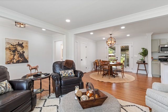 living room featuring a notable chandelier, light wood-type flooring, and crown molding