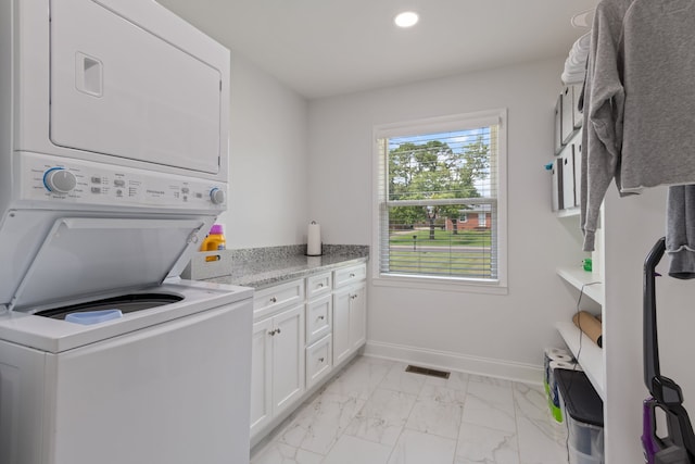 clothes washing area with cabinets, light tile patterned floors, and stacked washer / drying machine