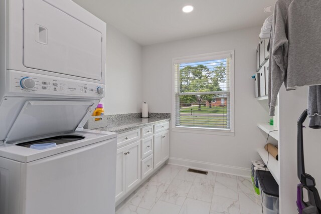clothes washing area featuring visible vents, marble finish floor, stacked washer and clothes dryer, cabinet space, and baseboards