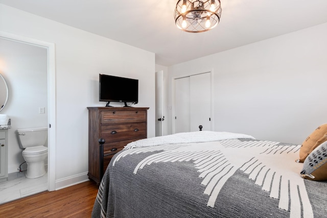 bedroom featuring baseboards, an inviting chandelier, wood finished floors, a closet, and ensuite bath