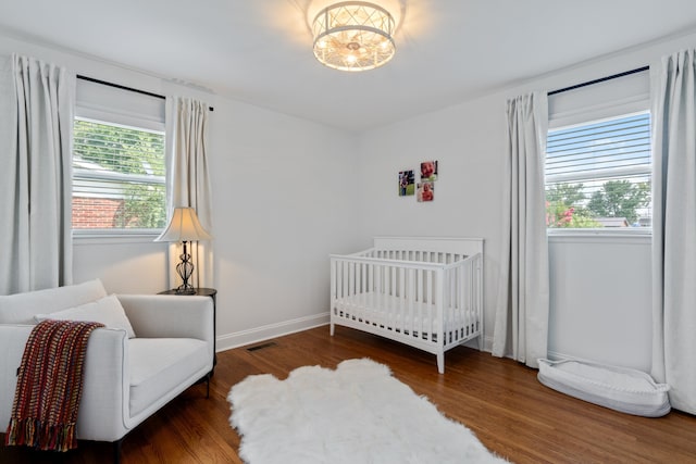 bedroom with wood-type flooring, multiple windows, and a crib