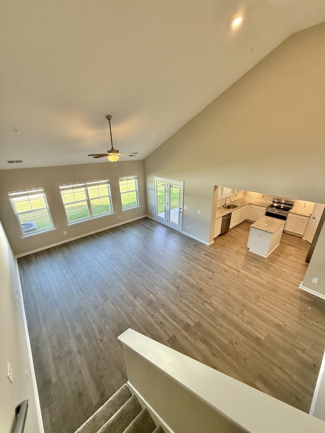 unfurnished living room with sink, ceiling fan, lofted ceiling, and light wood-type flooring