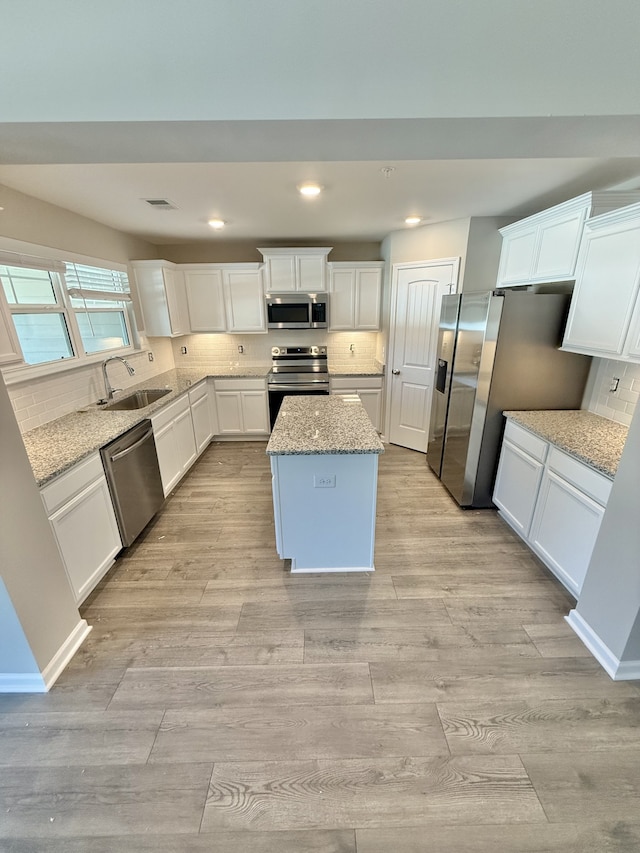 kitchen with a center island, white cabinetry, light stone countertops, and stainless steel appliances