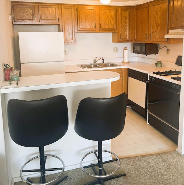 kitchen featuring white appliances, brown cabinets, light countertops, under cabinet range hood, and a sink