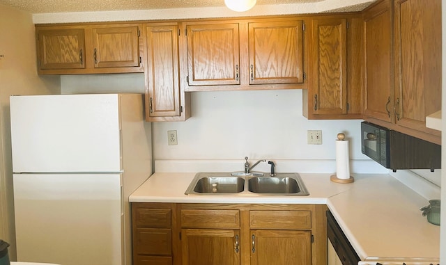 kitchen with brown cabinetry, freestanding refrigerator, light countertops, and a sink