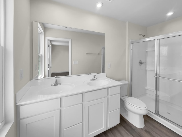 bathroom with double sink vanity, toilet, a shower with shower door, and hardwood / wood-style floors