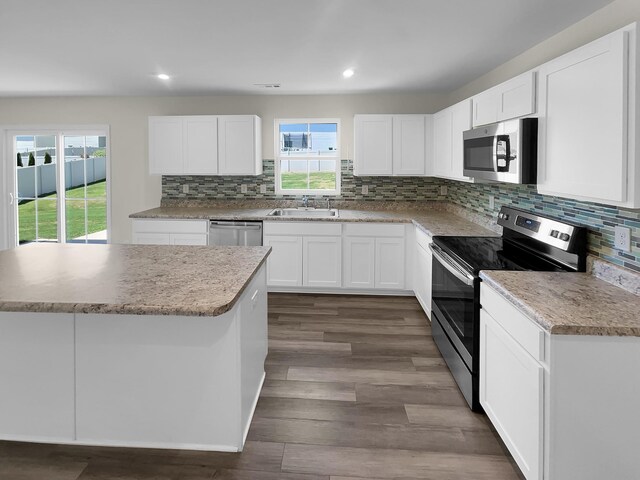 kitchen with sink, dark wood-type flooring, appliances with stainless steel finishes, white cabinetry, and a center island