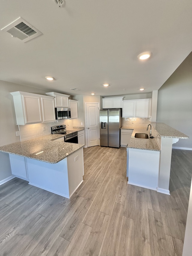 kitchen with appliances with stainless steel finishes, sink, kitchen peninsula, and white cabinets