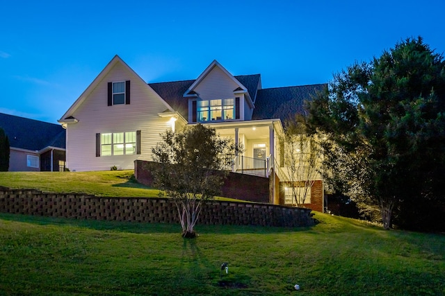 back house at dusk featuring a yard and covered porch