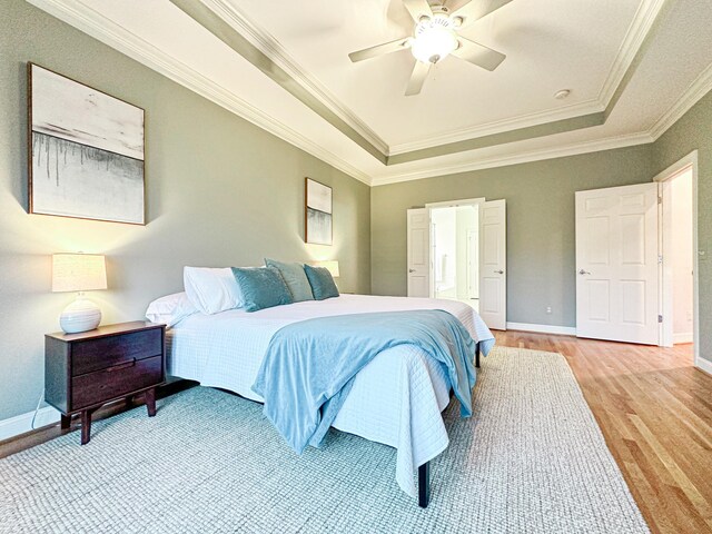 bedroom featuring light hardwood / wood-style flooring, ornamental molding, a tray ceiling, and ceiling fan