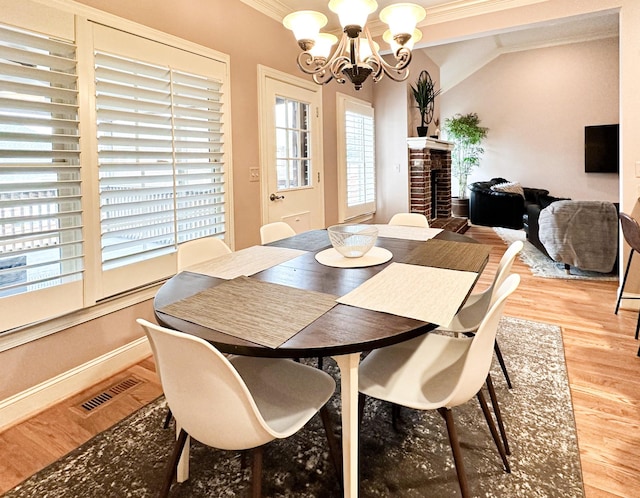 dining space with a fireplace, lofted ceiling, ornamental molding, a notable chandelier, and light hardwood / wood-style floors