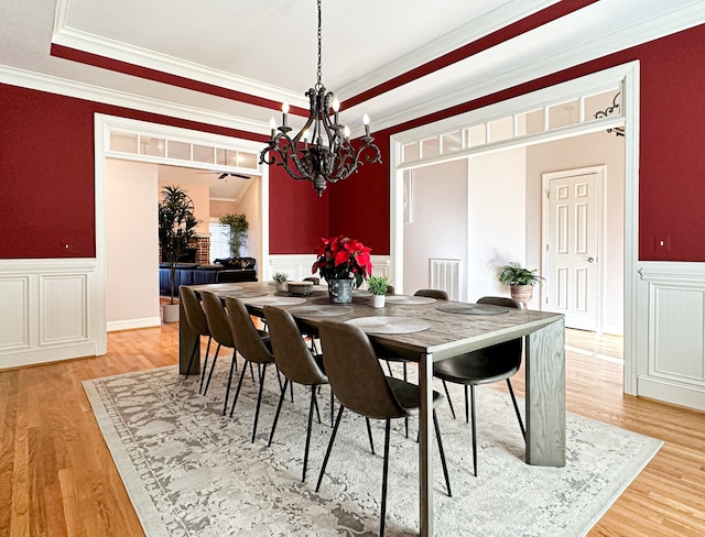 dining room with a tray ceiling, light wood-type flooring, crown molding, and an inviting chandelier