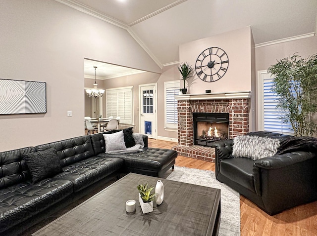 living room with vaulted ceiling, a brick fireplace, ornamental molding, a notable chandelier, and light hardwood / wood-style floors