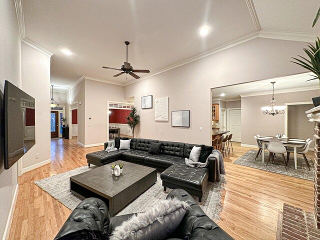 living room with vaulted ceiling, ceiling fan with notable chandelier, hardwood / wood-style floors, and crown molding