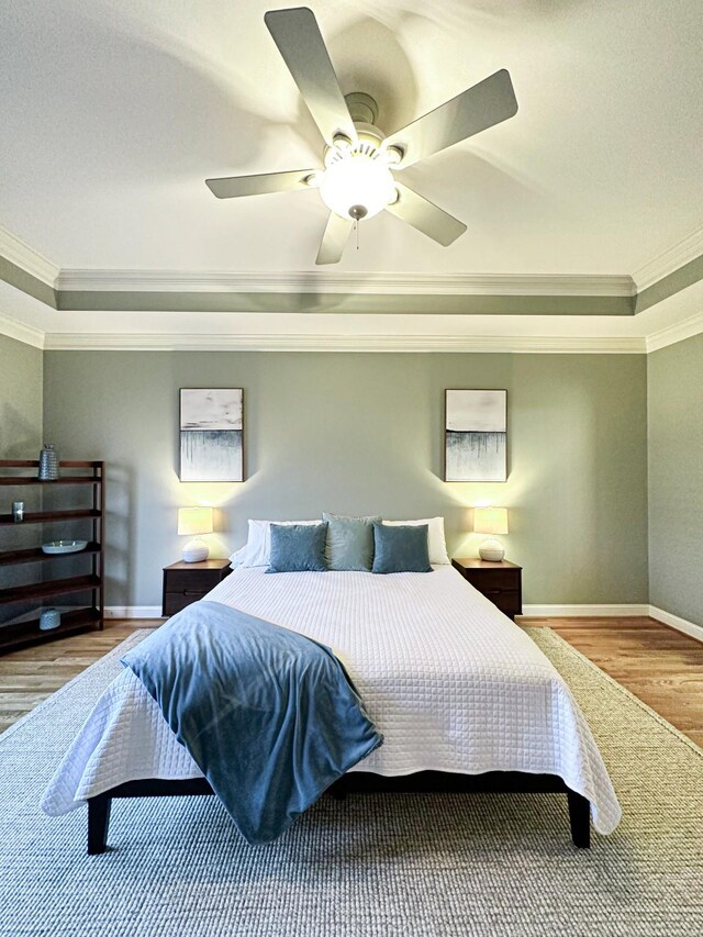 bedroom with crown molding, light hardwood / wood-style floors, a raised ceiling, and ceiling fan