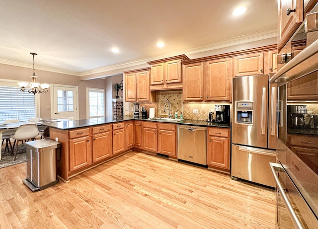 kitchen with appliances with stainless steel finishes, decorative light fixtures, sink, kitchen peninsula, and light hardwood / wood-style flooring