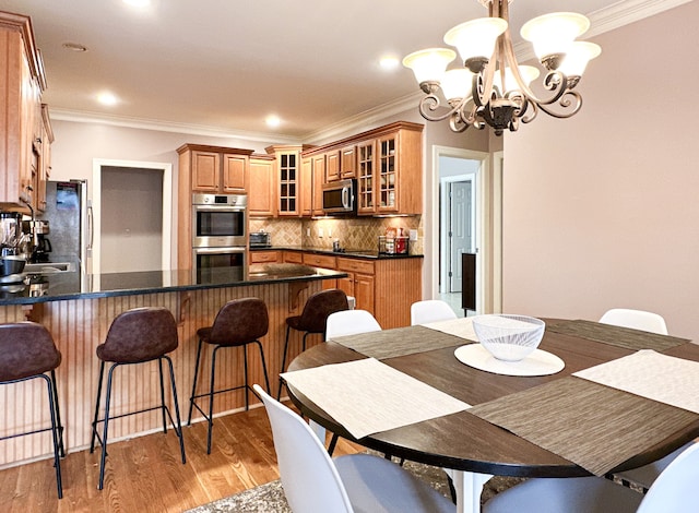 dining space featuring sink, light hardwood / wood-style flooring, ornamental molding, and an inviting chandelier