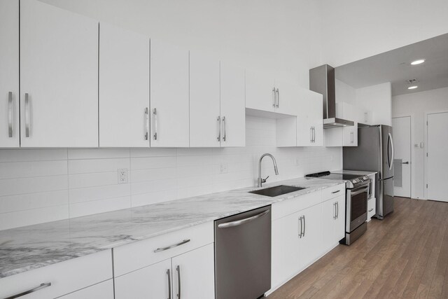 kitchen with appliances with stainless steel finishes, white cabinets, backsplash, sink, and wall chimney range hood