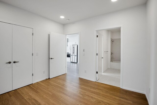 unfurnished bedroom with stainless steel fridge, light hardwood / wood-style flooring, ensuite bath, and a closet