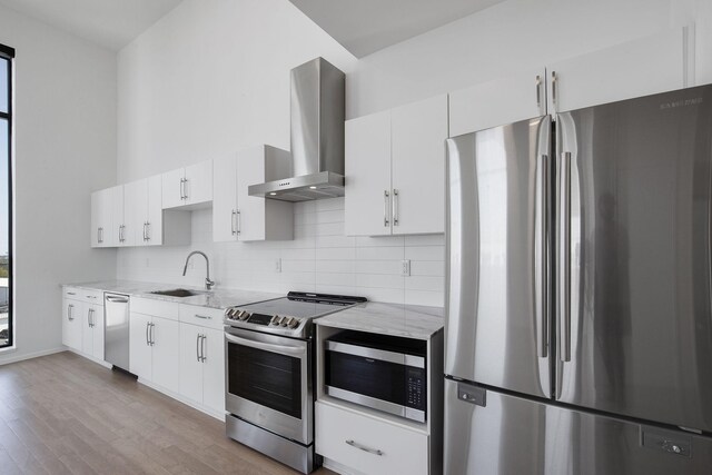 kitchen with stainless steel appliances, light stone countertops, light hardwood / wood-style flooring, decorative backsplash, and wall chimney range hood