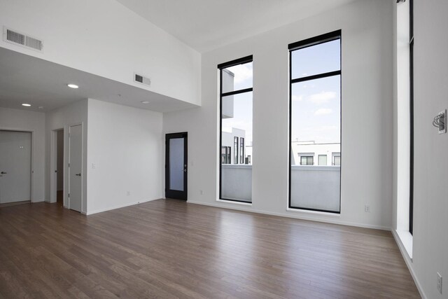 unfurnished room with a towering ceiling, hardwood / wood-style flooring, and a wealth of natural light