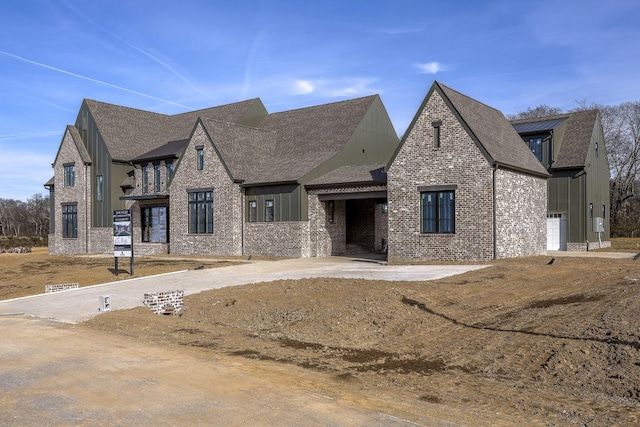 view of front facade with board and batten siding, concrete driveway, brick siding, and roof with shingles