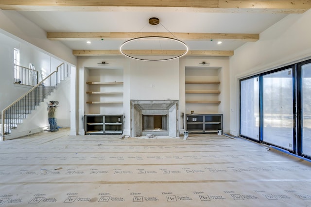 unfurnished living room with built in shelves, beamed ceiling, and wood finished floors