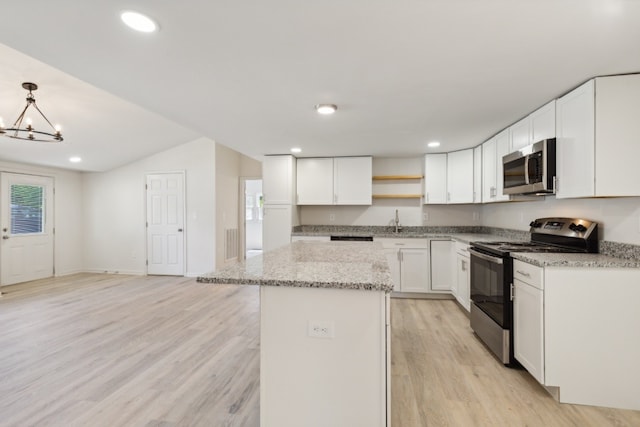 kitchen featuring light wood-type flooring, appliances with stainless steel finishes, white cabinetry, light stone counters, and decorative light fixtures