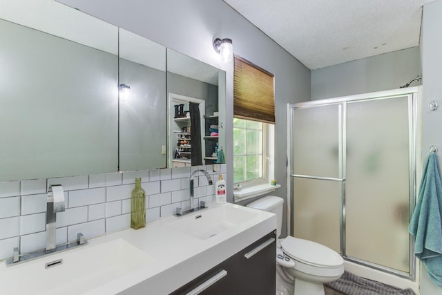 bathroom featuring decorative backsplash, vanity, toilet, a shower with door, and a textured ceiling