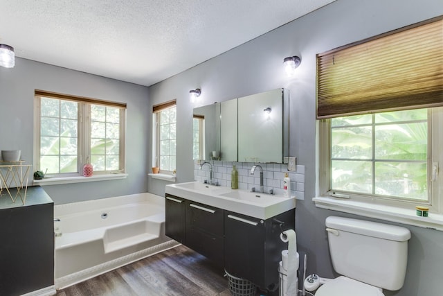 bathroom with wood-type flooring, a textured ceiling, vanity, a tub, and decorative backsplash