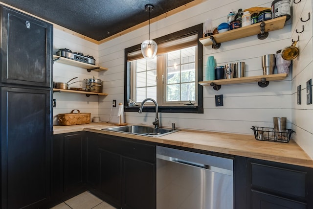 kitchen with light tile patterned flooring, sink, wooden counters, hanging light fixtures, and stainless steel dishwasher