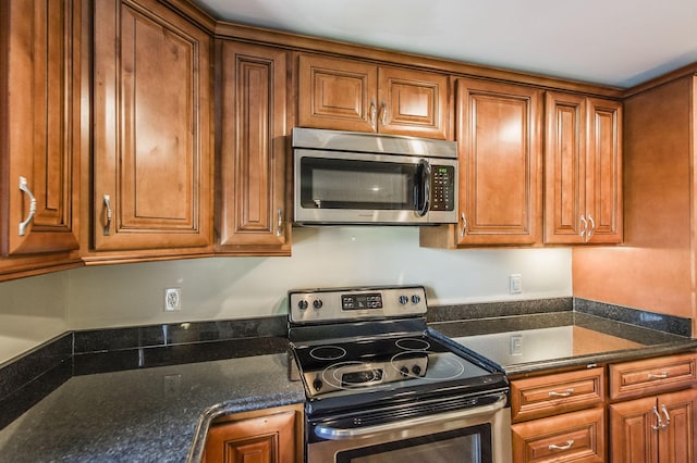 kitchen featuring stainless steel appliances, built in desk, and brown cabinetry