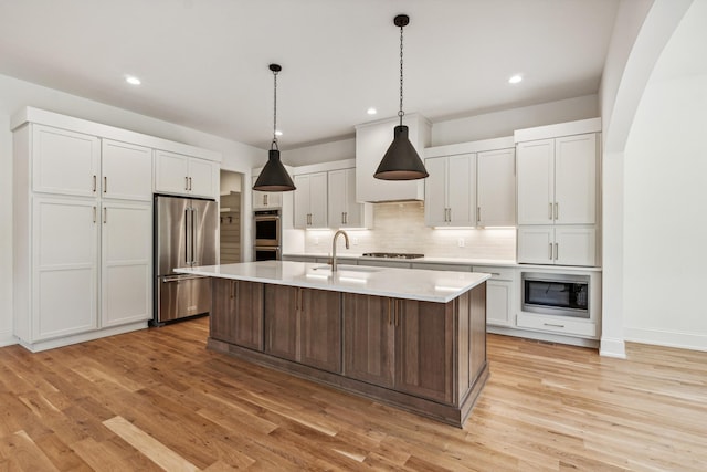 kitchen with sink, appliances with stainless steel finishes, white cabinetry, a kitchen island with sink, and decorative light fixtures