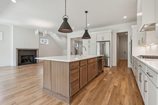 kitchen with a tile fireplace, light hardwood / wood-style flooring, white cabinetry, and a kitchen island with sink