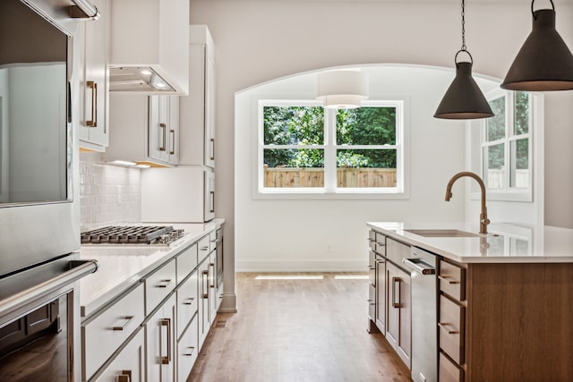 kitchen with premium range hood, an island with sink, backsplash, double wall oven, and light hardwood / wood-style flooring