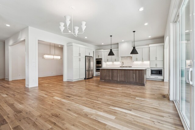 kitchen featuring pendant lighting, stainless steel appliances, a kitchen island with sink, white cabinetry, and light hardwood / wood-style flooring