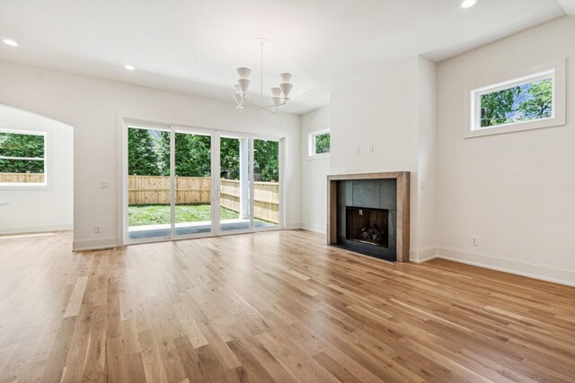 unfurnished living room featuring a tiled fireplace, light wood-type flooring, and a chandelier