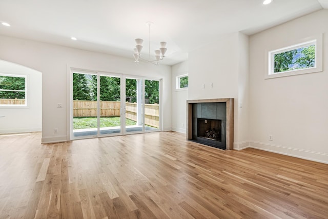 unfurnished living room with light hardwood / wood-style floors, a tile fireplace, and a notable chandelier