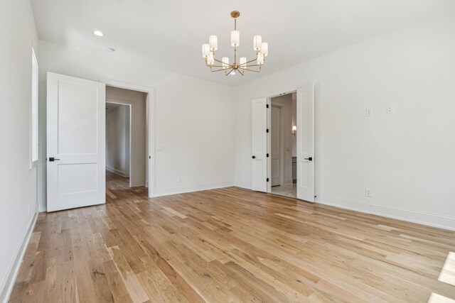 spare room featuring light wood-type flooring and a chandelier