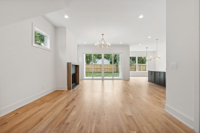 unfurnished living room with an inviting chandelier, plenty of natural light, and light hardwood / wood-style floors